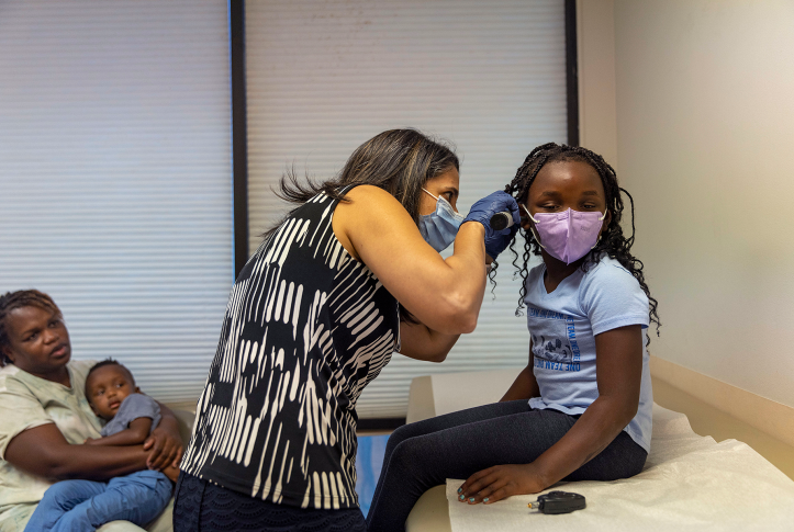 Doctor in mask examines girl in mask's ear on table